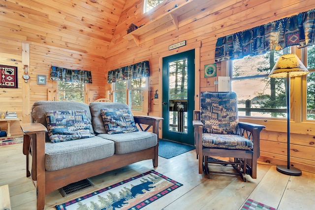 living room featuring a wealth of natural light, light hardwood / wood-style flooring, high vaulted ceiling, and wood walls