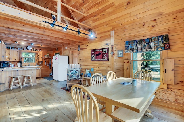 dining room featuring wood walls, light hardwood / wood-style floors, wooden ceiling, and beamed ceiling