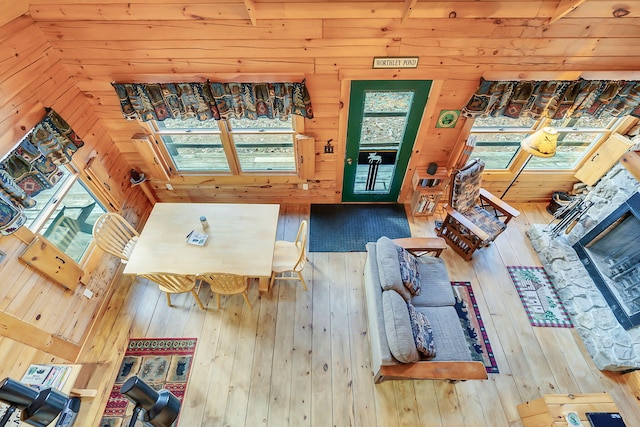 living room featuring hardwood / wood-style flooring, a stone fireplace, a healthy amount of sunlight, and wood walls