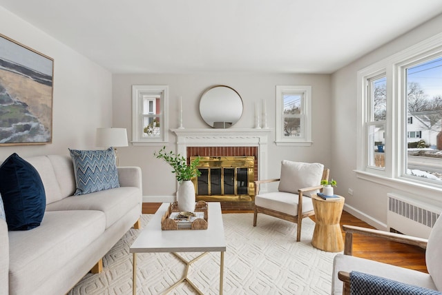 living room with a brick fireplace, radiator heating unit, and light wood-type flooring