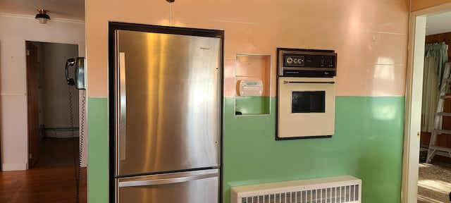 kitchen with oven, stainless steel fridge, radiator heating unit, and dark hardwood / wood-style floors