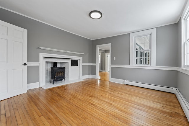 unfurnished living room featuring a wood stove, crown molding, a baseboard heating unit, and light wood-type flooring