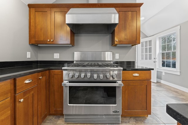 kitchen with dark stone counters, wall chimney exhaust hood, light tile patterned flooring, and high end stainless steel range oven