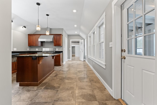 kitchen featuring wall chimney exhaust hood, pendant lighting, lofted ceiling, a kitchen bar, and stainless steel stove