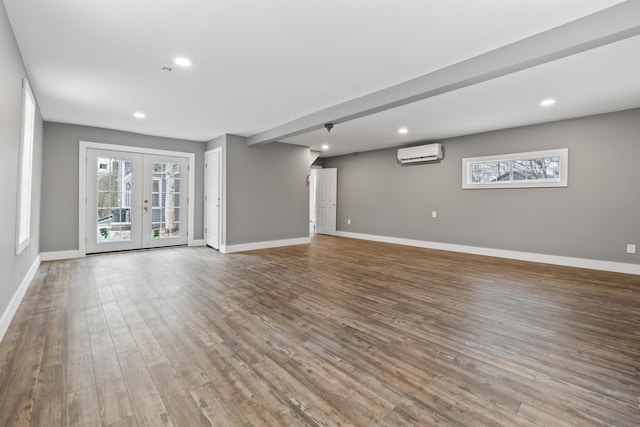 unfurnished living room with hardwood / wood-style flooring, a wall unit AC, and french doors