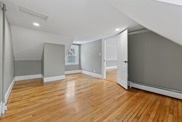 additional living space with baseboard heating, vaulted ceiling, and light wood-type flooring