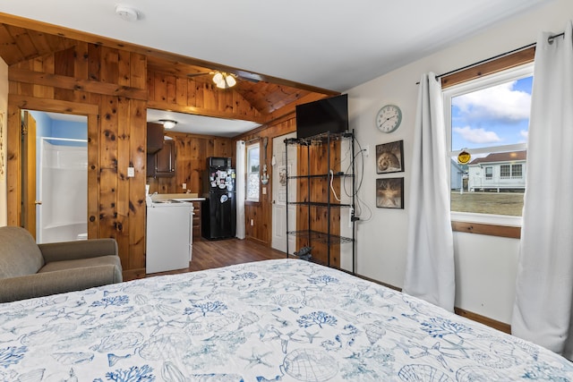 bedroom with black refrigerator, dark hardwood / wood-style flooring, vaulted ceiling, connected bathroom, and wood walls