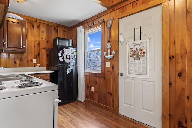 kitchen with black appliances, wood walls, and light hardwood / wood-style floors