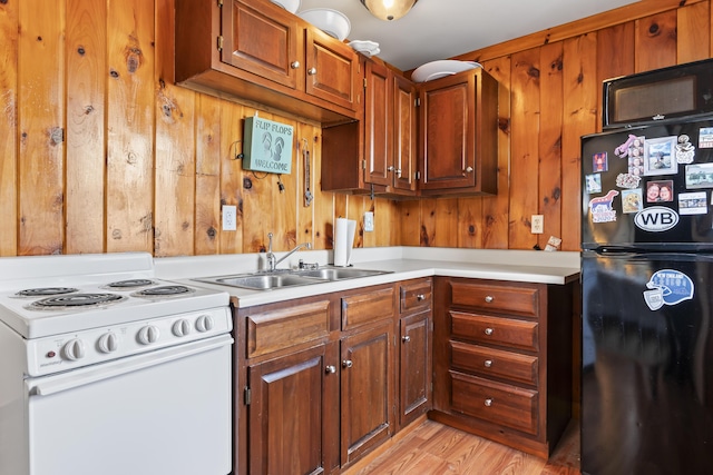 kitchen featuring sink, black fridge, white range with electric stovetop, light hardwood / wood-style floors, and wooden walls