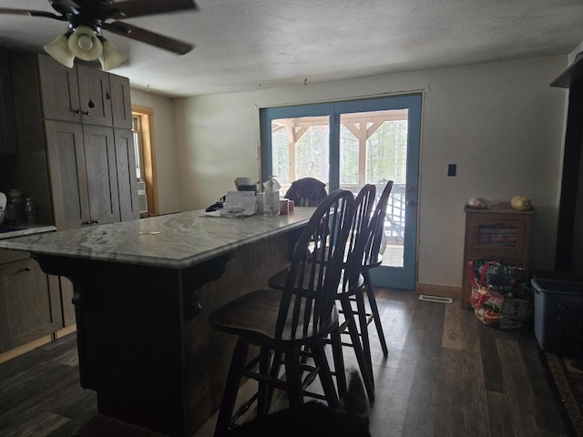 kitchen with a kitchen bar, a textured ceiling, a center island, and dark wood-type flooring