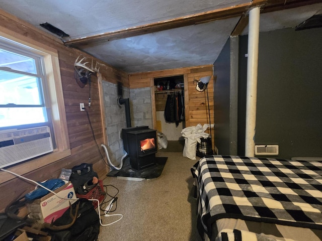 carpeted bedroom with a wood stove, a closet, and wooden walls