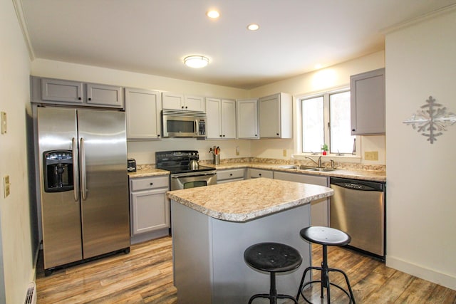 kitchen with a kitchen bar, appliances with stainless steel finishes, sink, light hardwood / wood-style flooring, and a center island