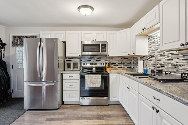 kitchen with appliances with stainless steel finishes, backsplash, sink, white cabinets, and hardwood / wood-style floors