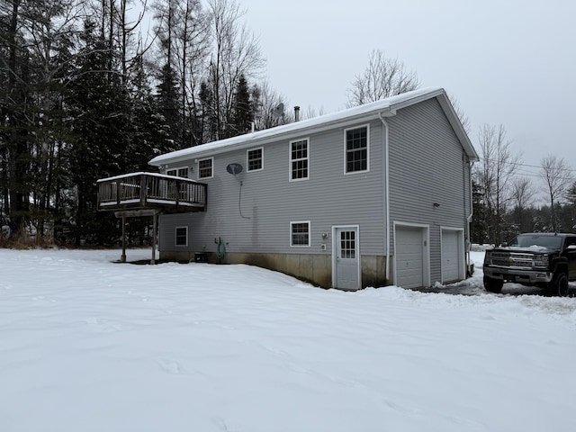 snow covered back of property featuring a garage and a wooden deck