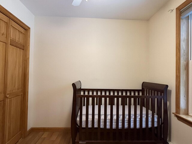 bedroom featuring ceiling fan, a nursery area, and wood-type flooring