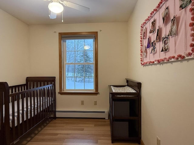 bedroom featuring a nursery area, light hardwood / wood-style floors, ceiling fan, and a baseboard heating unit