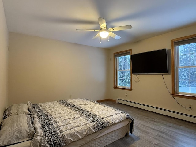 bedroom featuring ceiling fan, a baseboard heating unit, wood-type flooring, and multiple windows