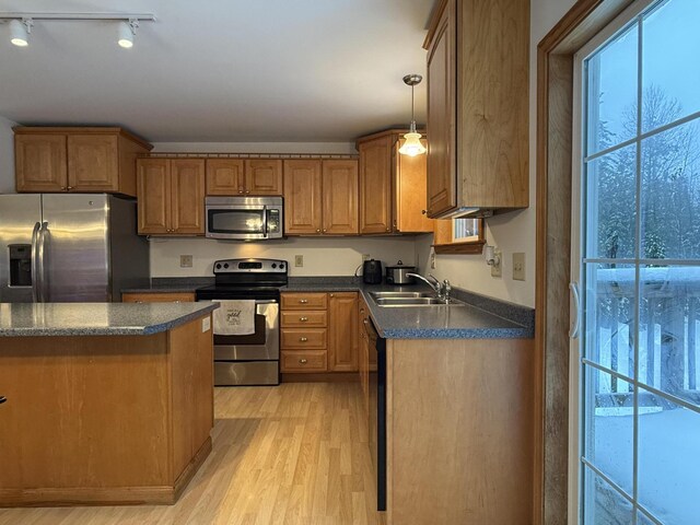 kitchen with appliances with stainless steel finishes, track lighting, sink, light hardwood / wood-style flooring, and hanging light fixtures