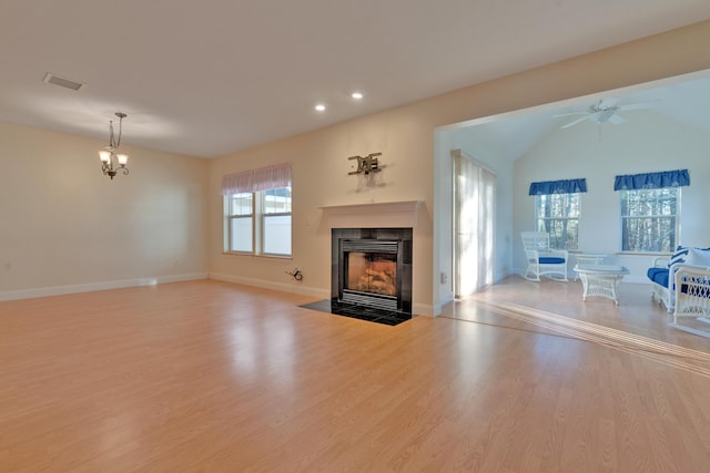 living room featuring lofted ceiling, light wood-type flooring, a fireplace, and ceiling fan with notable chandelier