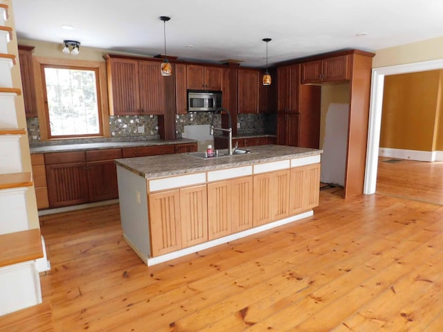 kitchen with backsplash, sink, pendant lighting, a center island with sink, and light hardwood / wood-style flooring