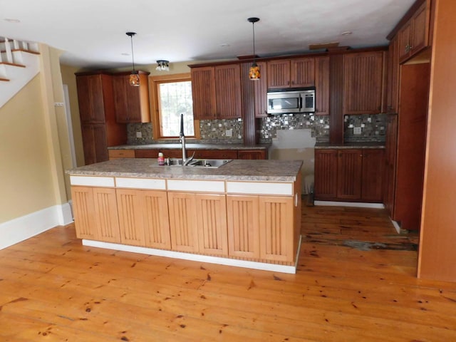 kitchen featuring decorative backsplash, a kitchen island with sink, light hardwood / wood-style flooring, and hanging light fixtures