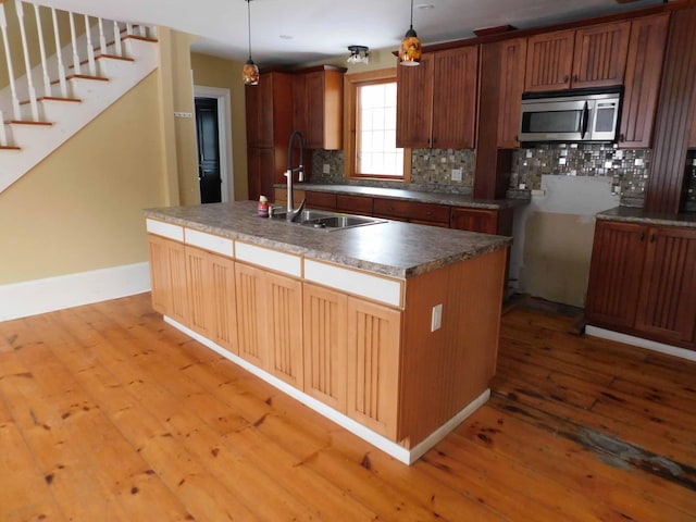 kitchen featuring decorative backsplash, a kitchen island with sink, sink, decorative light fixtures, and light hardwood / wood-style floors