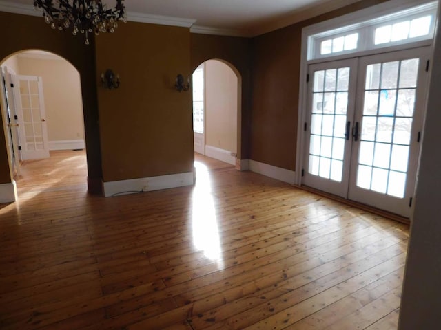 spare room with a notable chandelier, light hardwood / wood-style floors, crown molding, and french doors