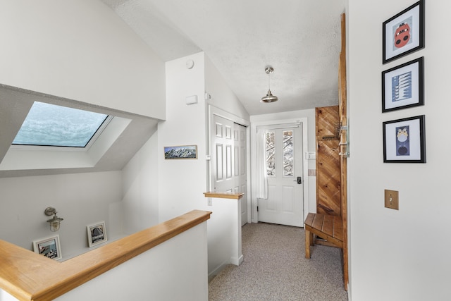 hallway with lofted ceiling with skylight, light colored carpet, and a textured ceiling