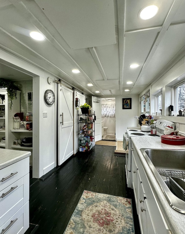 kitchen featuring dark hardwood / wood-style flooring, sink, a barn door, white cabinetry, and range with electric stovetop