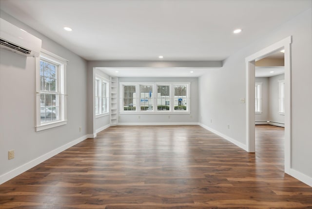 unfurnished living room with dark hardwood / wood-style floors, an AC wall unit, baseboard heating, and a healthy amount of sunlight