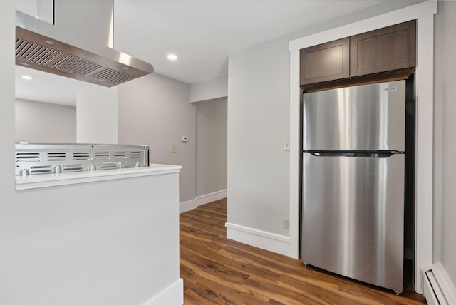 kitchen with dark wood-type flooring, exhaust hood, a baseboard radiator, dark brown cabinetry, and stainless steel refrigerator