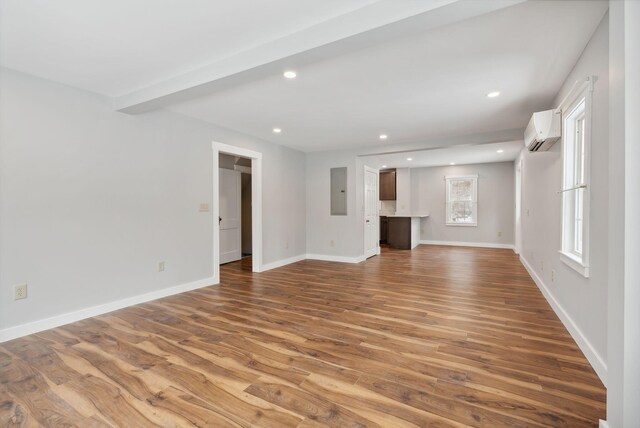 unfurnished living room featuring beamed ceiling, hardwood / wood-style floors, electric panel, and a wall unit AC