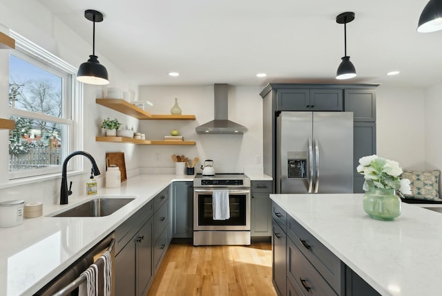 kitchen featuring pendant lighting, wall chimney range hood, sink, stainless steel appliances, and light hardwood / wood-style floors