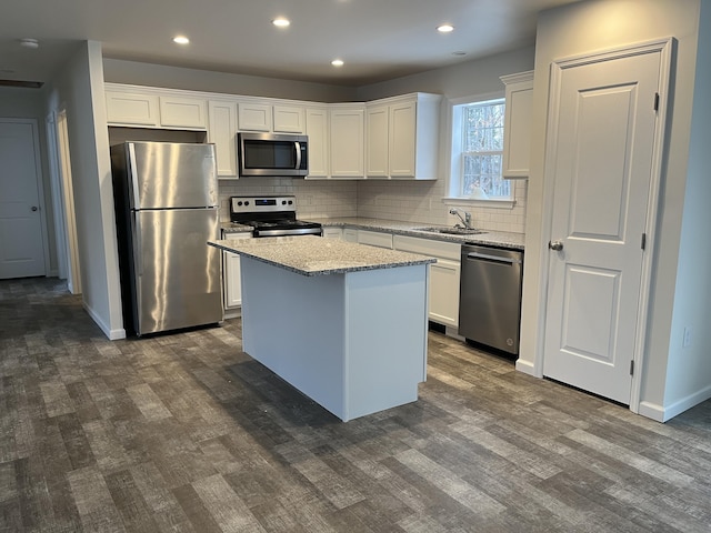 kitchen with white cabinets, a kitchen island, light stone counters, and appliances with stainless steel finishes