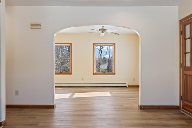 empty room featuring baseboard heating, ceiling fan, and light wood-type flooring