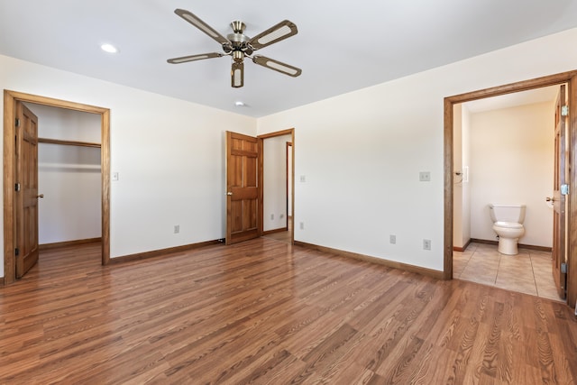 unfurnished bedroom with ensuite bathroom, a walk in closet, ceiling fan, and light wood-type flooring