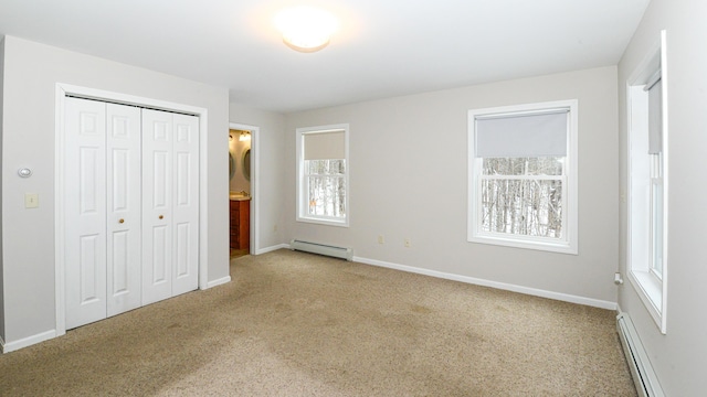 unfurnished bedroom featuring baseboard heating, ensuite bath, a closet, and light colored carpet