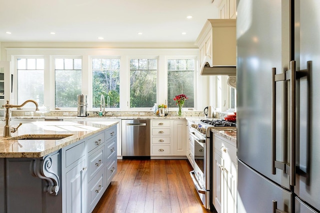 kitchen with light stone counters, high end appliances, dark wood-type flooring, sink, and white cabinets