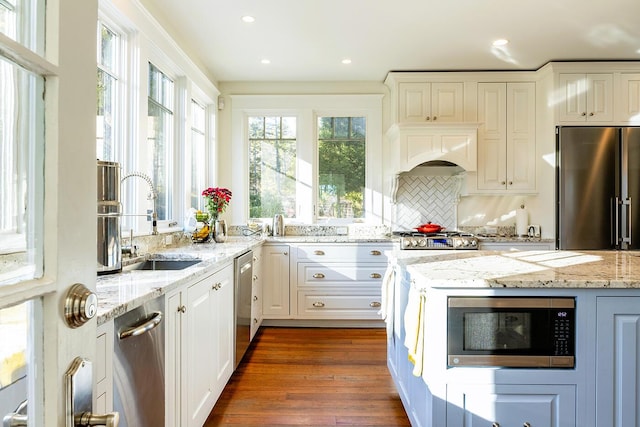 kitchen featuring dark wood-type flooring, sink, appliances with stainless steel finishes, light stone counters, and custom range hood