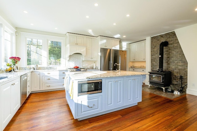 kitchen with light stone counters, stainless steel appliances, hardwood / wood-style flooring, a center island with sink, and white cabinetry