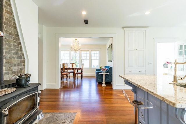 kitchen with a kitchen breakfast bar, light stone counters, dark hardwood / wood-style floors, and an inviting chandelier