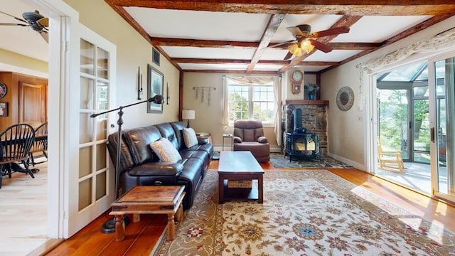 living room featuring beam ceiling, hardwood / wood-style flooring, a wood stove, and ceiling fan