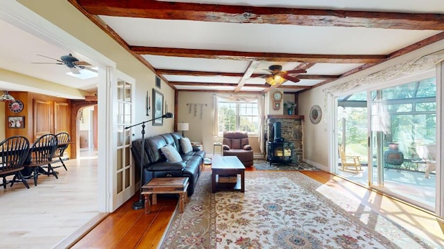 living room featuring a wood stove, ceiling fan, beamed ceiling, and light hardwood / wood-style floors