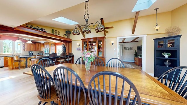 dining space featuring lofted ceiling with skylight, sink, and light wood-type flooring