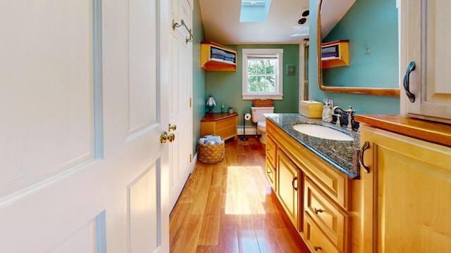 bathroom featuring a skylight, vanity, a baseboard heating unit, hardwood / wood-style floors, and toilet