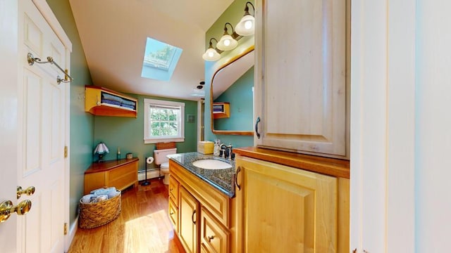 bathroom with a skylight, vanity, a baseboard radiator, hardwood / wood-style floors, and toilet