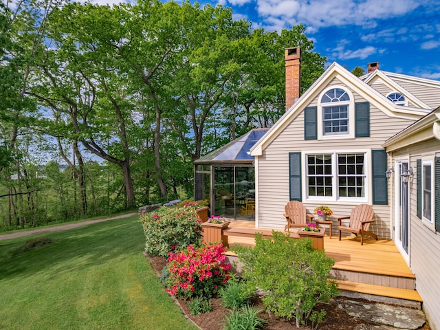 rear view of property with a wooden deck, a sunroom, and a yard