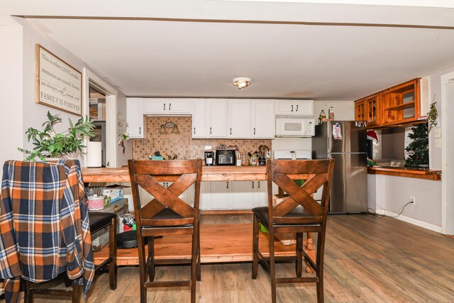 kitchen with hardwood / wood-style flooring, decorative backsplash, stainless steel fridge, and white cabinetry