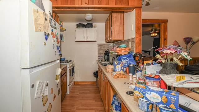 kitchen with stainless steel gas stove, decorative backsplash, light hardwood / wood-style flooring, and white fridge