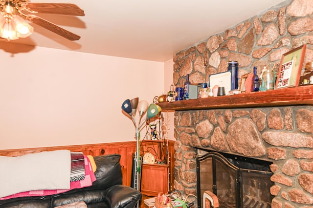 living room featuring ceiling fan, a stone fireplace, and wooden walls